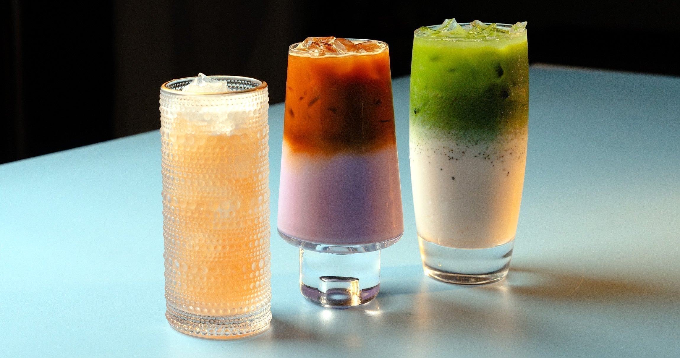 Three drinks sit on a blue table, each different from the other.