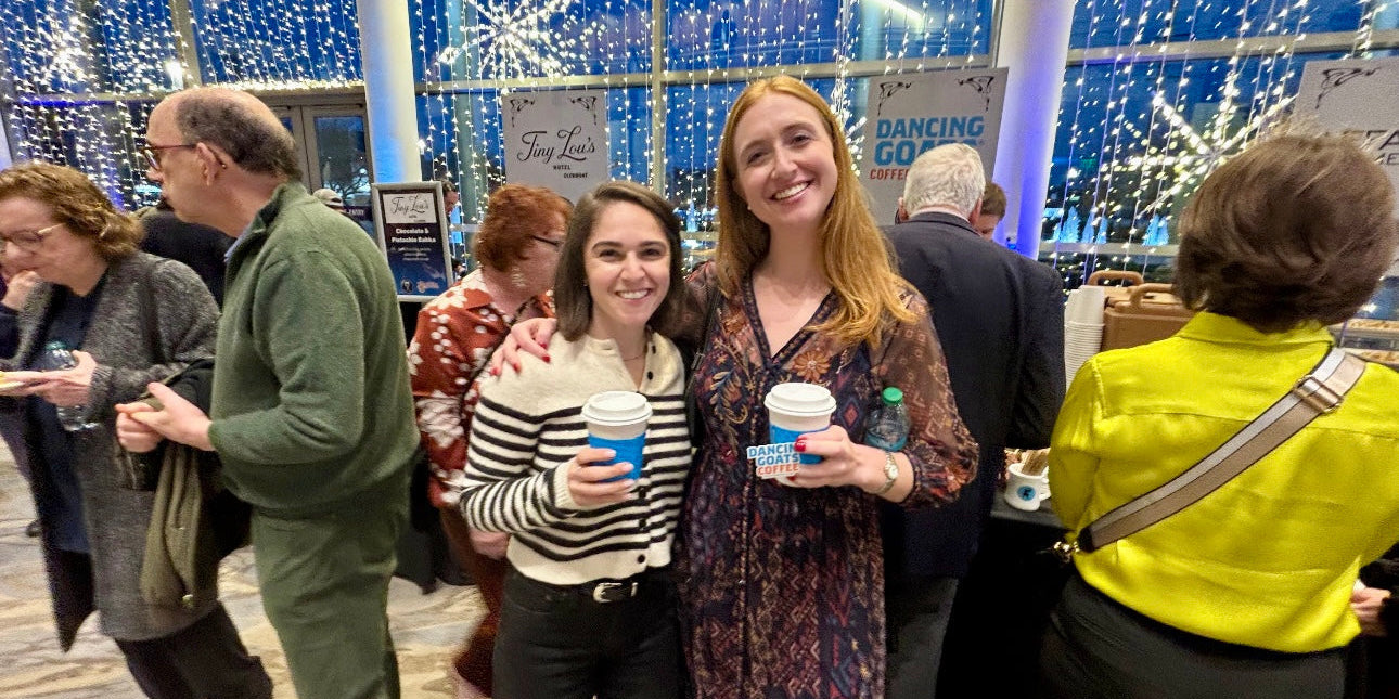 2 women holding coffee cups in front of a booth and backdrop