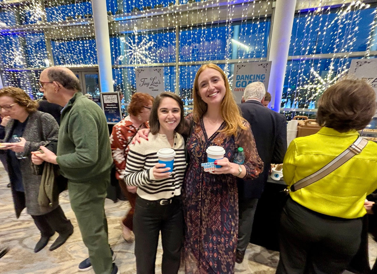 2 women holding coffee cups in front of a booth and backdrop