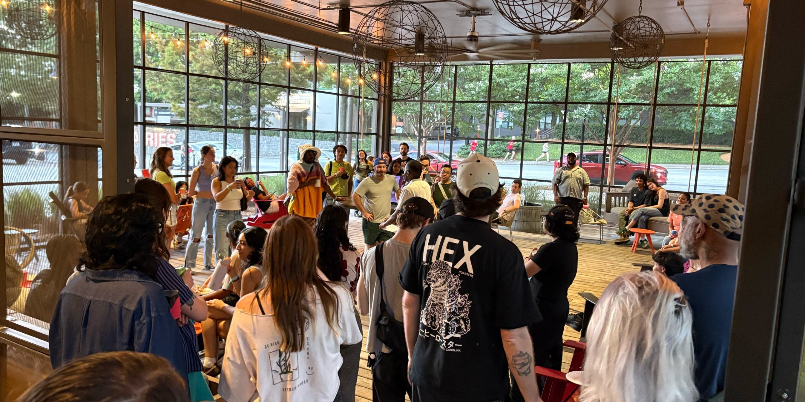 A large crowd gathers on a covered patio with wire globe lights and floor-to-ceiling windows to watch the Atlanta Throwdown latte art competition.