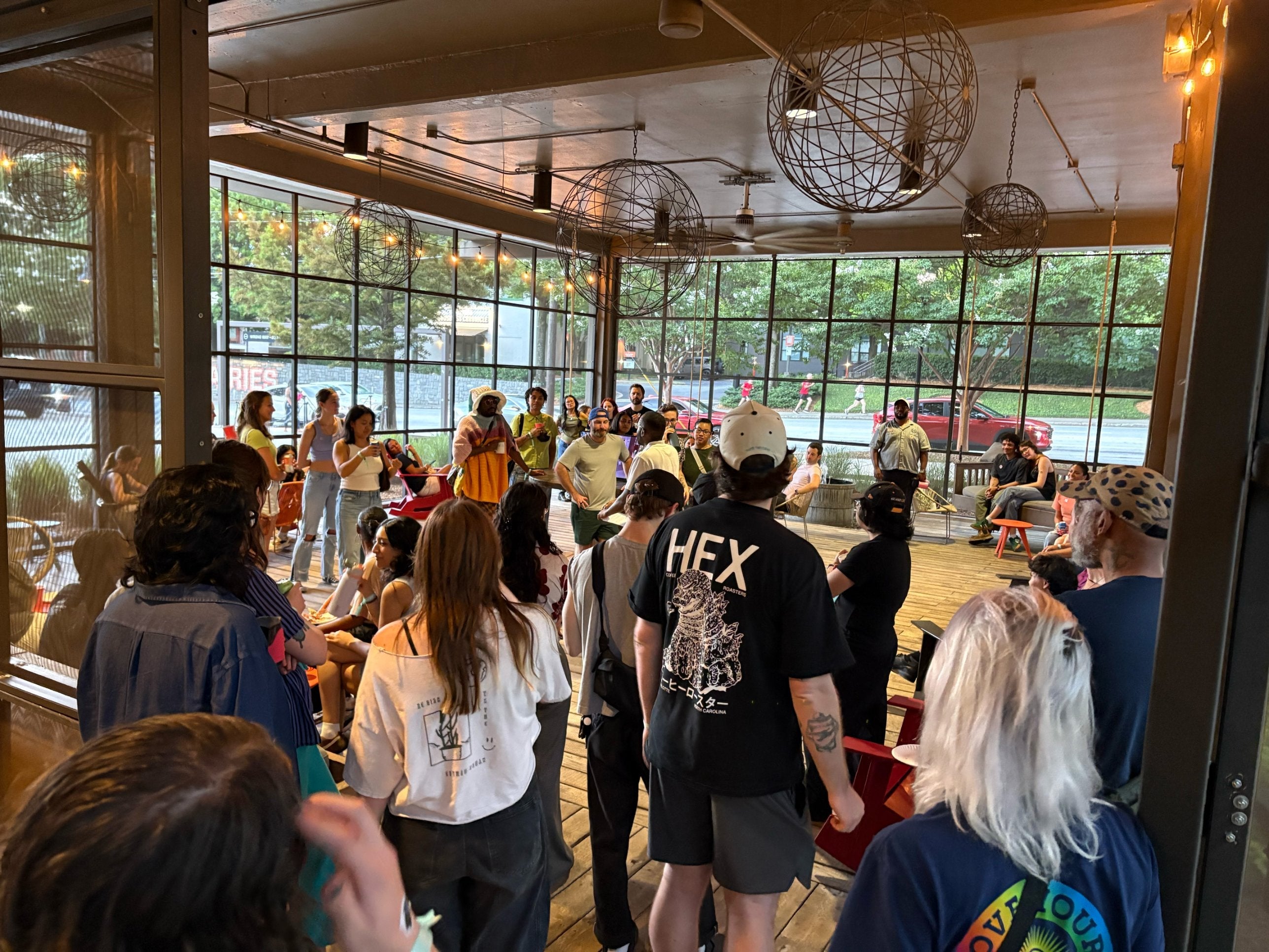 A large crowd gathers on a covered patio with wire globe lights and floor-to-ceiling windows to watch the Atlanta Throwdown latte art competition.