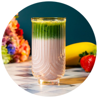 Glass of layered green and pink drink with fruits in the background