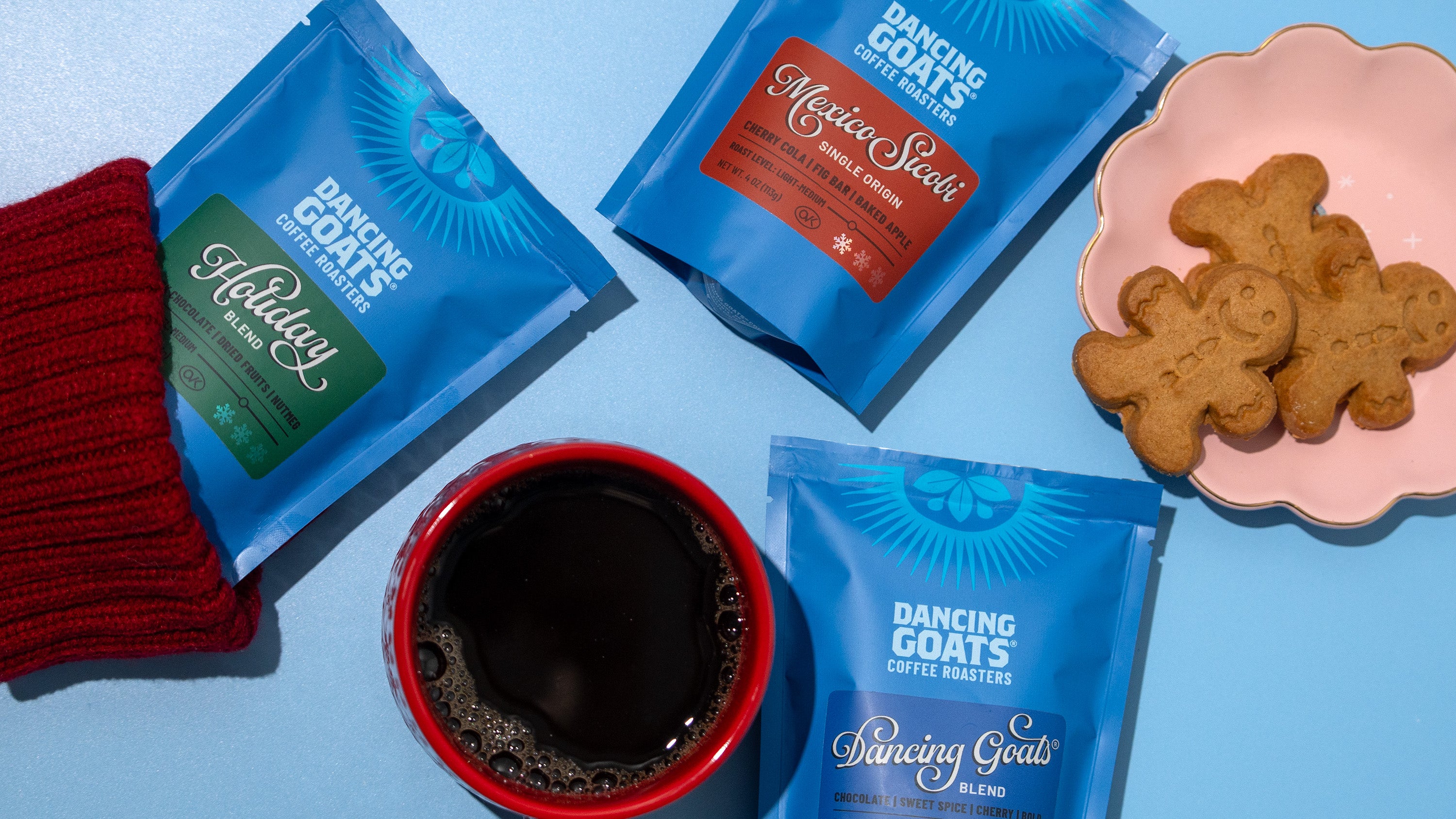Dancing Goats coffee packages with a cup of coffee and cookies on a blue background
