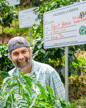Man standing in a coffee plantation with a sign in the background