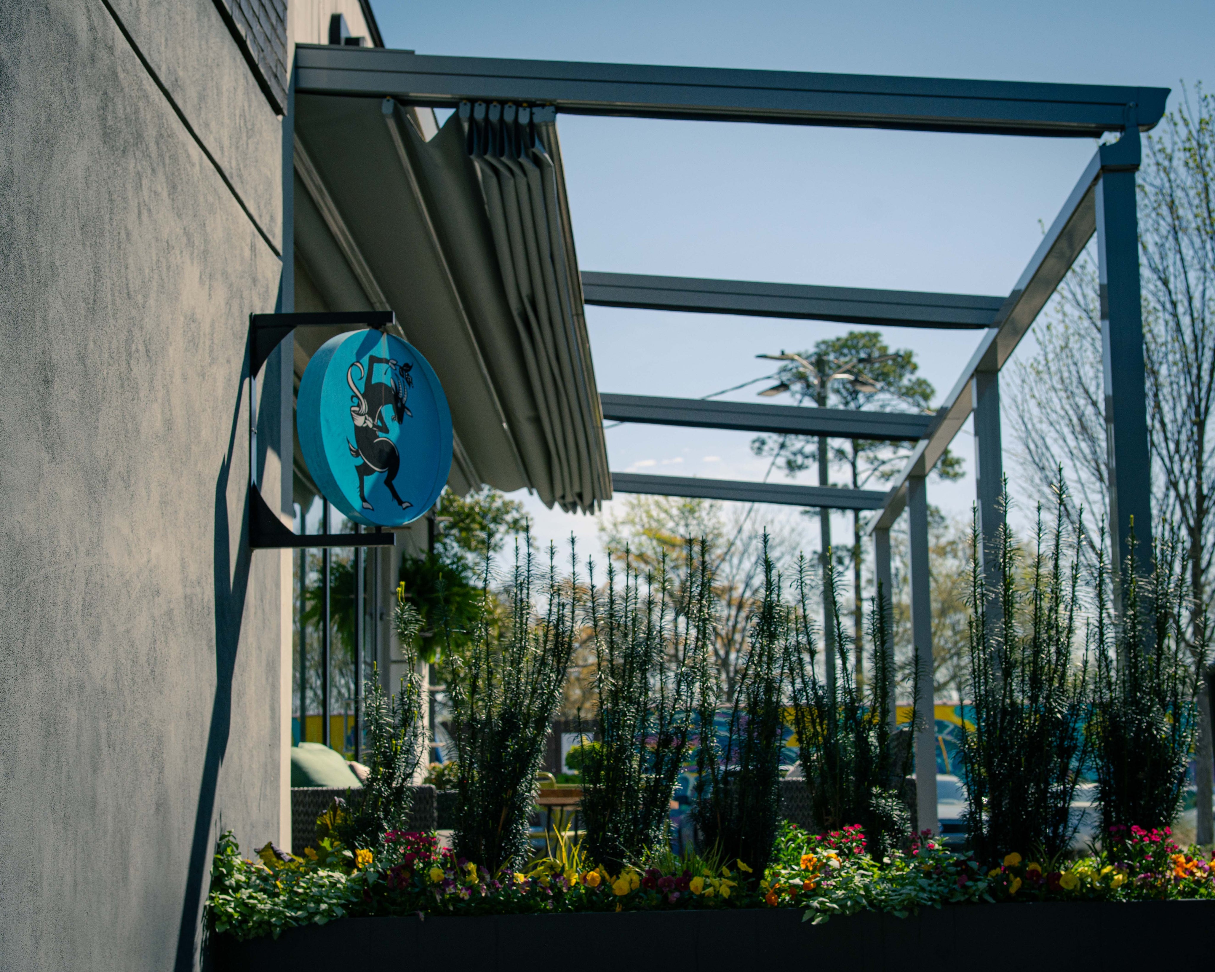 Outdoor setting with a blue circular sign on a building facade, surrounded by plants and flowers.