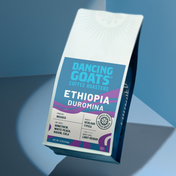 A bag of Dancing Goats Coffee Roasters Ethiopia Duromina coffee, shown at an angle on a blue and gray geometric background.