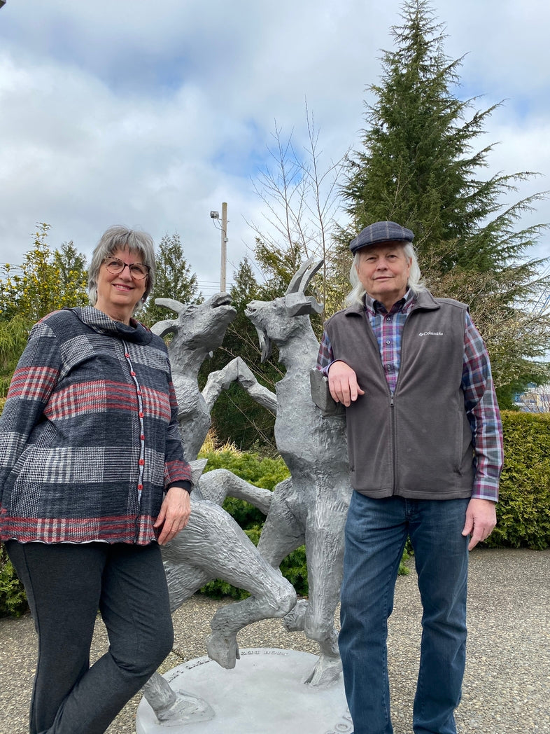Cherie and Larry standing in front of a sculpture of goats in a garden setting.