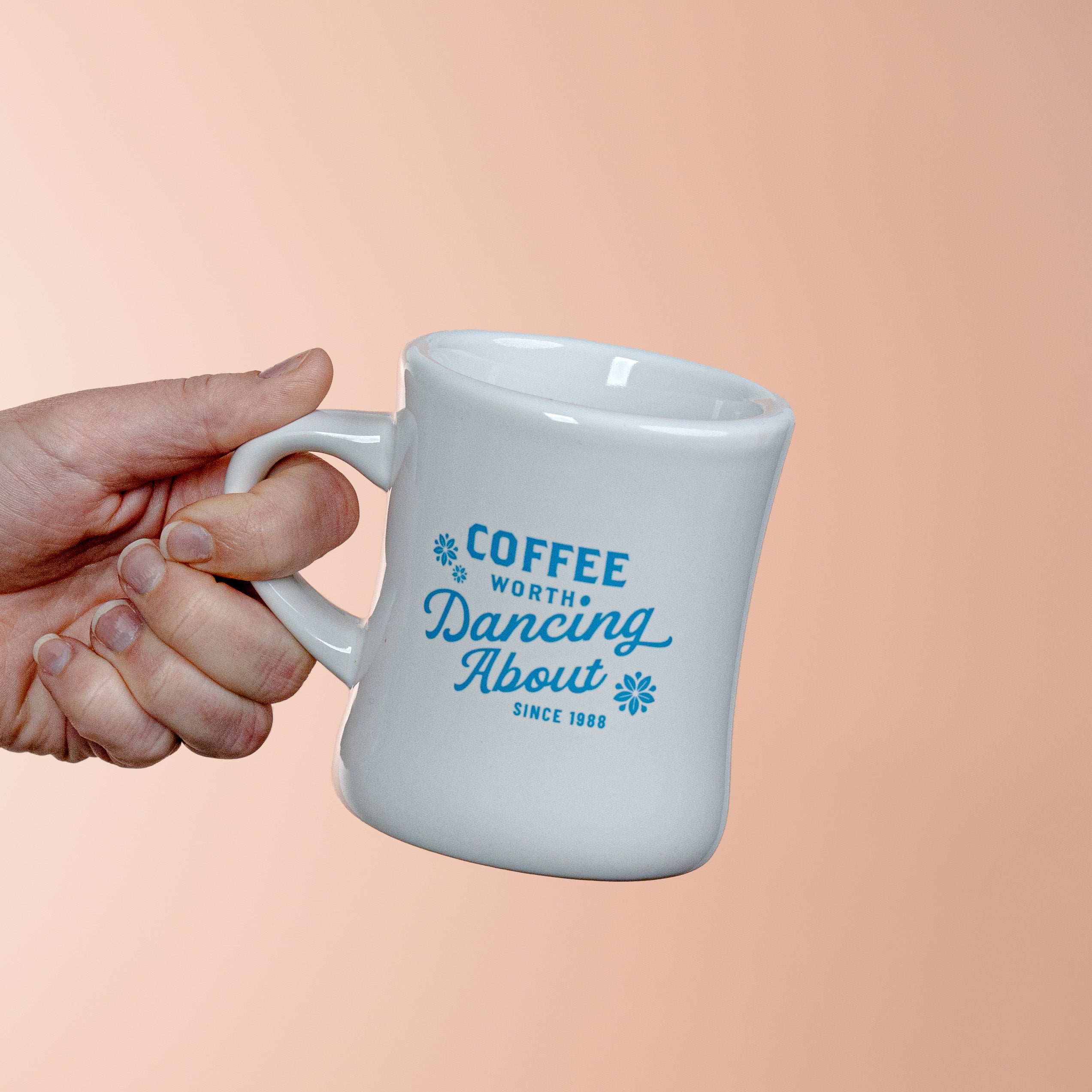 White mug with blue text held by a hand against a peach background