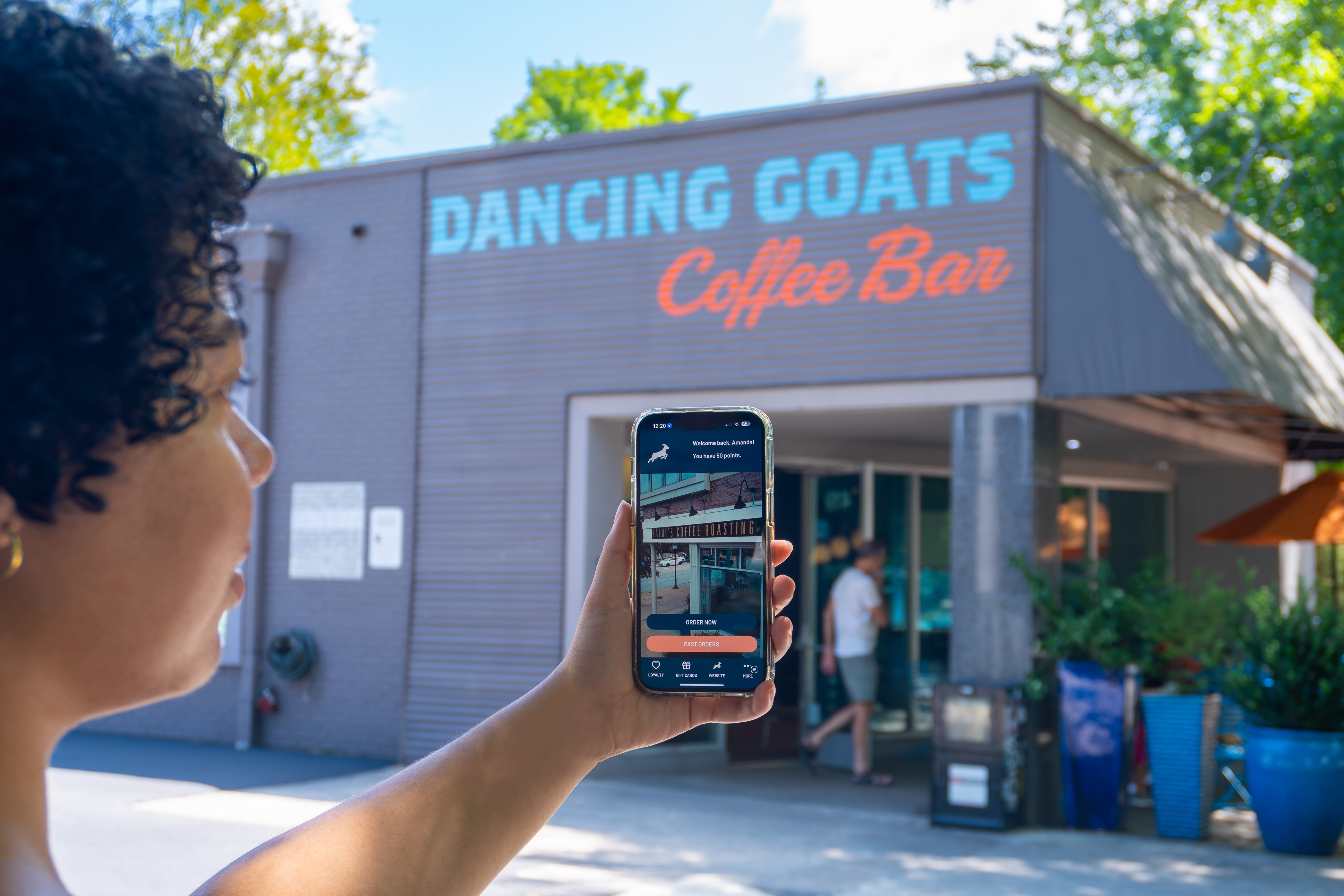 Person holding a phone with a map app in front of 'Dancing Goats Coffee Bar'