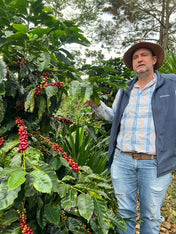 Man standing among coffee trees with red coffee beans on a farm