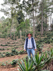 Man standing in a coffee plantation with trees and plants around