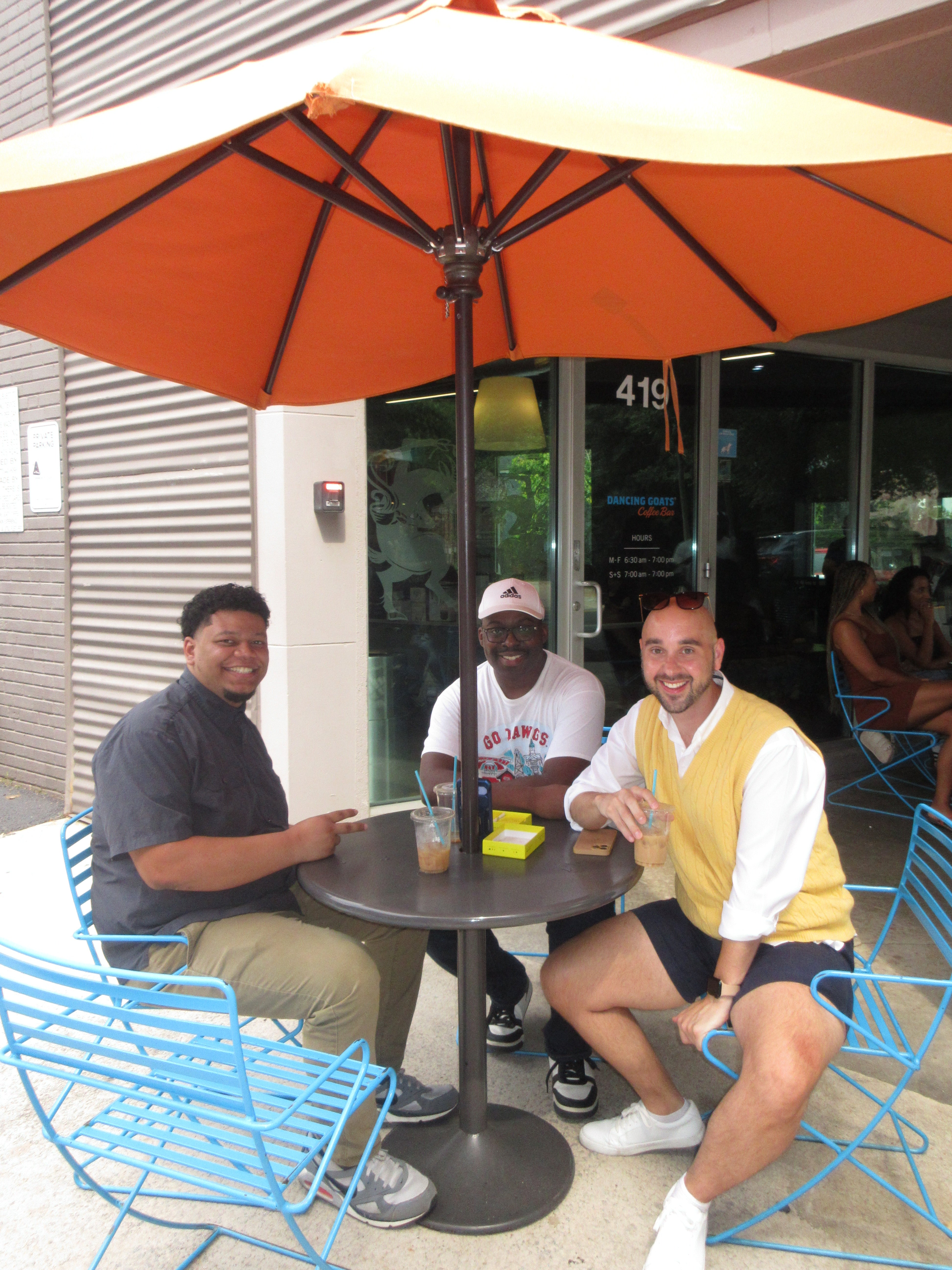 Three people sitting at a table with an orange umbrella, reflected in a glass door.