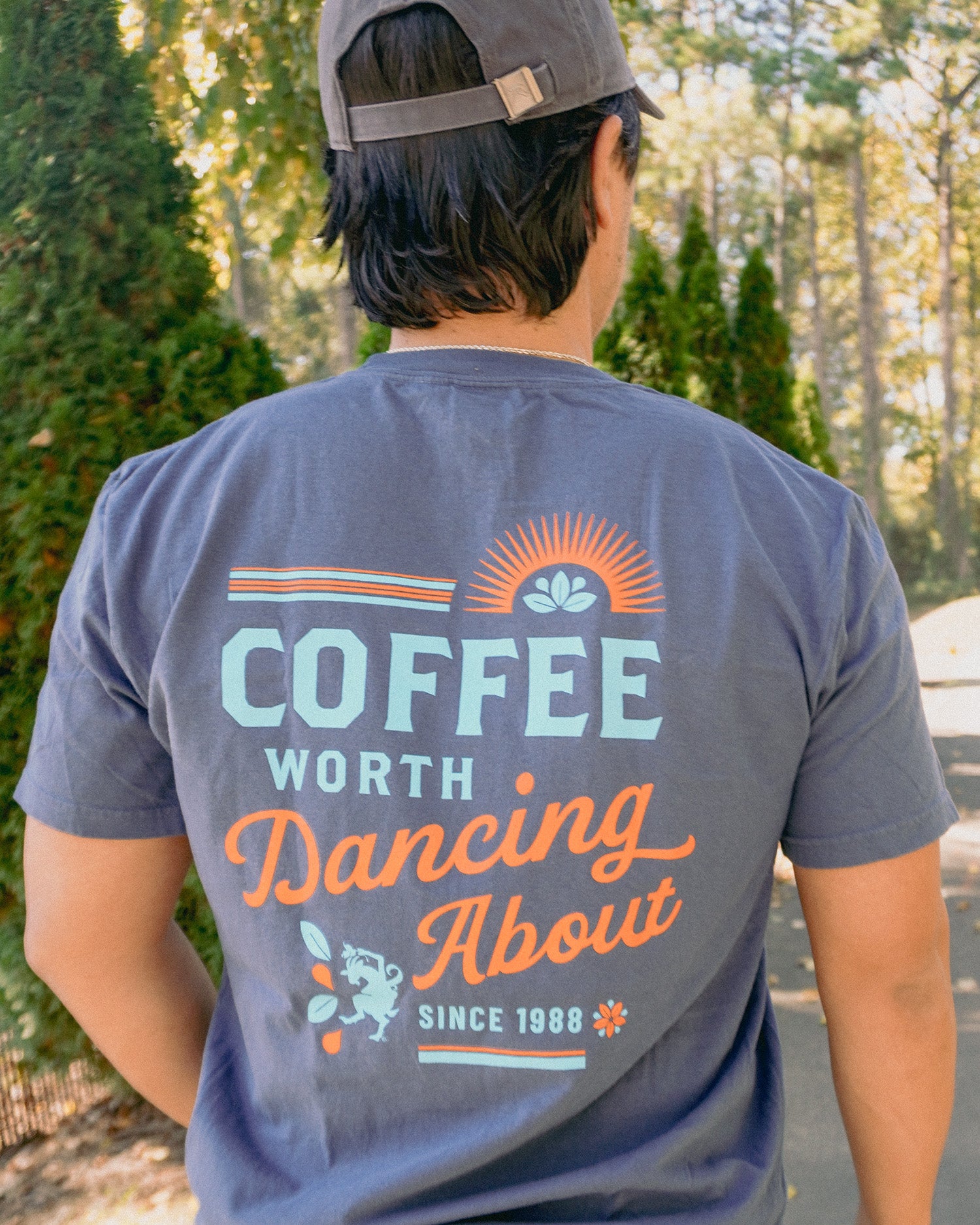 Person wearing a t-shirt with 'Coffee Worth Dancing About' text outdoors.