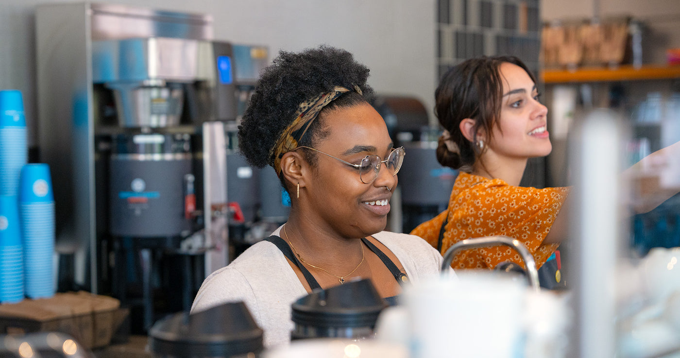 Two baristas smile as they work the espresso bar in Midtown