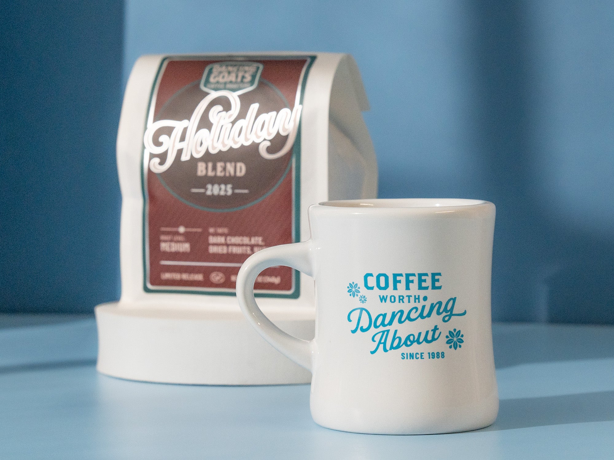 White mug with blue text and a package of holiday coffee on a blue background