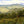 Panoramic view of a lush green landscape with rolling hills and trees under a cloudy sky.